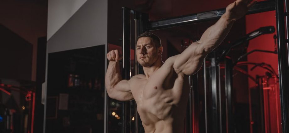 Strong and muscular man posing topless in a gym, showcasing fitness and strength.